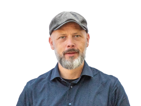 Een man met een baard, een grijze pet en een donker overhemd met kraag staat tegenover de camera tegen een eenvoudige achtergrond. Dit weerspiegelt de professionele stijl die je vaak op websites en webshops ziet.