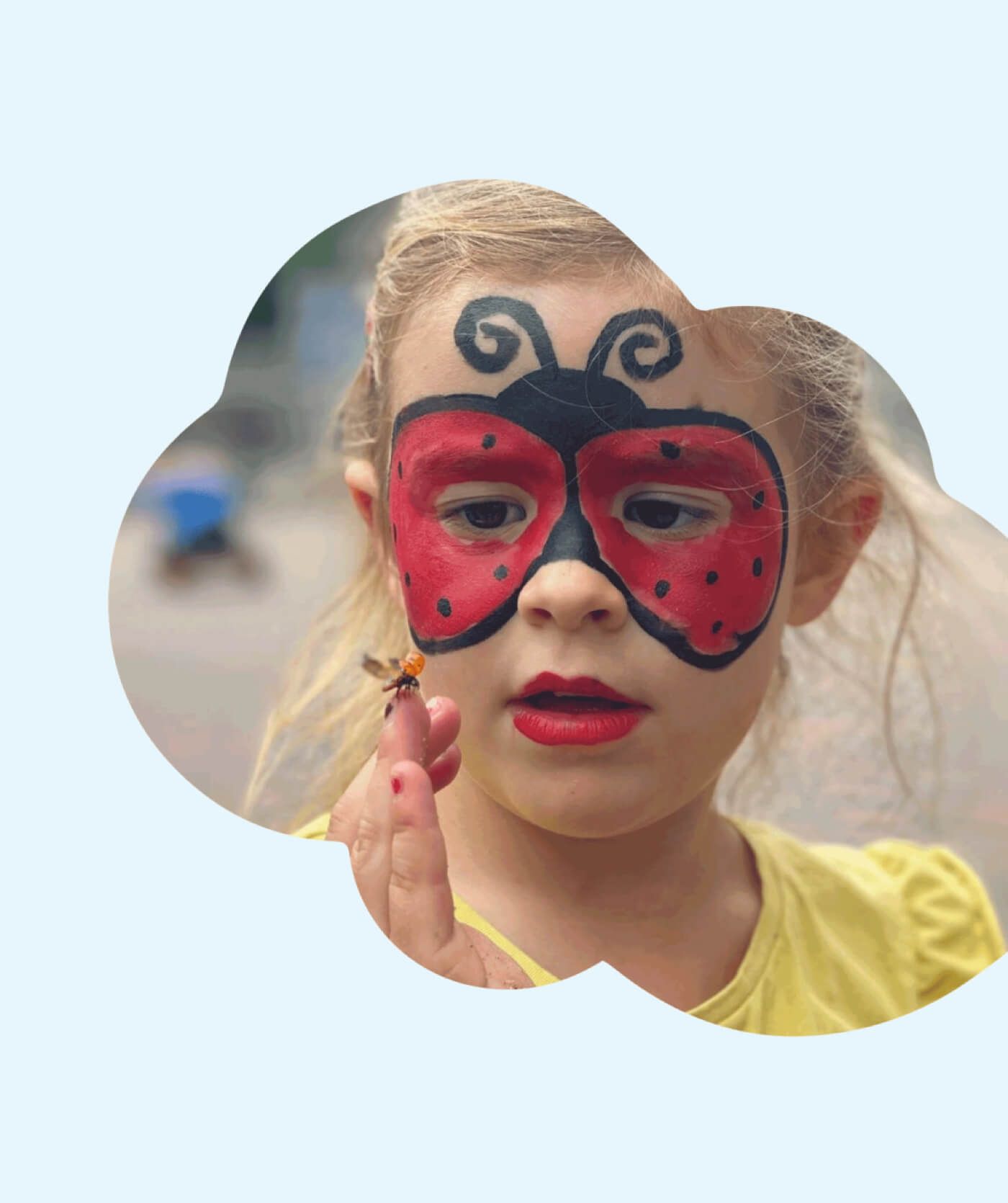 Een jong meisje dat haar gezicht heeft beschilderd met lieveheersbeestjes, kijkt aandachtig naar een echt lieveheersbeestje dat op haar vinger zit. Geboeid bladert ze door websites met leuke ideeën voor gezichtsverf.